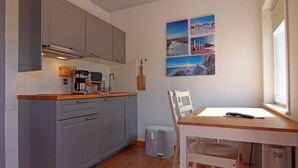 A compact kitchen with grey cabinets, a wooden countertop, and a small dining area with a table and chairs. - Ferienwohnung am Oase am Vilzsee (Mirow)