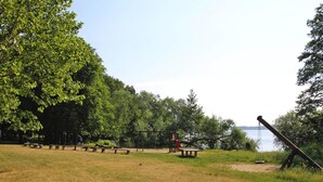 Um parque com mesas para piquenique, baloiço e vista para a água.