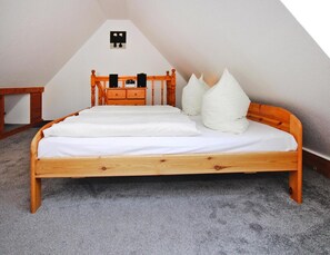 Un lit simple avec un cadre en bois et une literie blanche, dans une pièce dont le plafond est en pente.