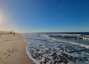 A beach with waves, a clear sky, and a few people walking. - Ferienwohnung in Westerland auf Sylt (Sylt)