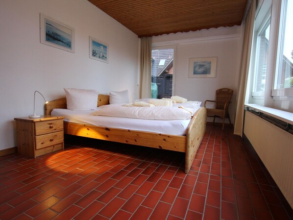 A bedroom with a wooden bed, a nightstand, a chair, and a window.