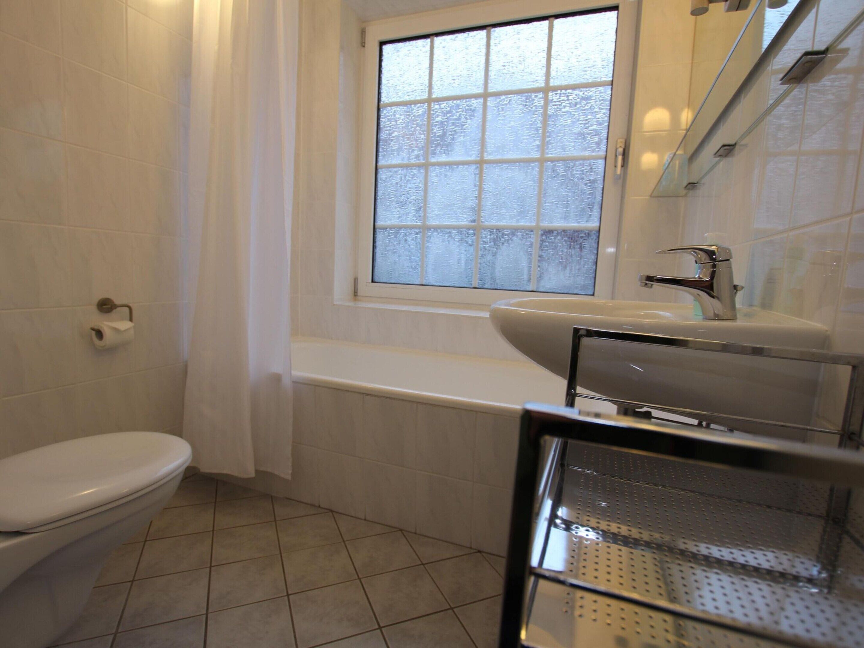 A bathroom with a toilet, a window, a bathtub, and a sink.