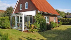 A two-story house with a red roof and a glass conservatory. - Ferienhaus Christina, Burhave (Butjadingen)