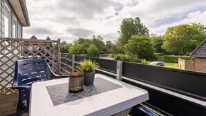 Un balcon avec une table, des chaises, un pot de fleurs et une vue sur un jardin et des maisons.
