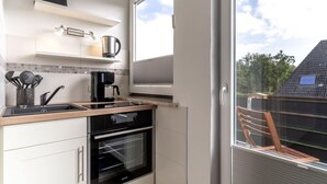 Une cuisine moderne équipée d’un four encastré, d’une machine à café et d’une fenêtre donnant sur un quartier résidentiel.