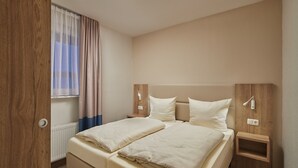 A double bed with two pillows, a bedside table with a lamp, a wooden headboard, and a window with curtains. - Appartements im Freizeitpark Weissenhauser Strand (Wangels)