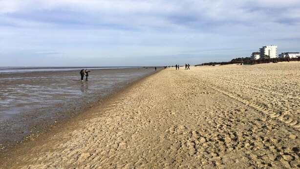 A sandy beach with people walking along the shore and buildings in the background. - Apartment, Cuxhaven (Cuxhaven)