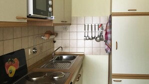 A kitchen with a stove, sink, microwave, and hanging utensils. - Apartment, Cuxhaven (Cuxhaven)