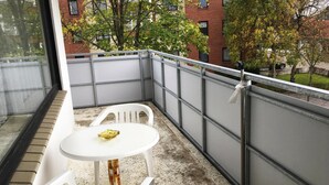 A balcony with a white table and chairs, a metal railing, and a view of a brick building and trees. - Apartment, Cuxhaven (Cuxhaven)