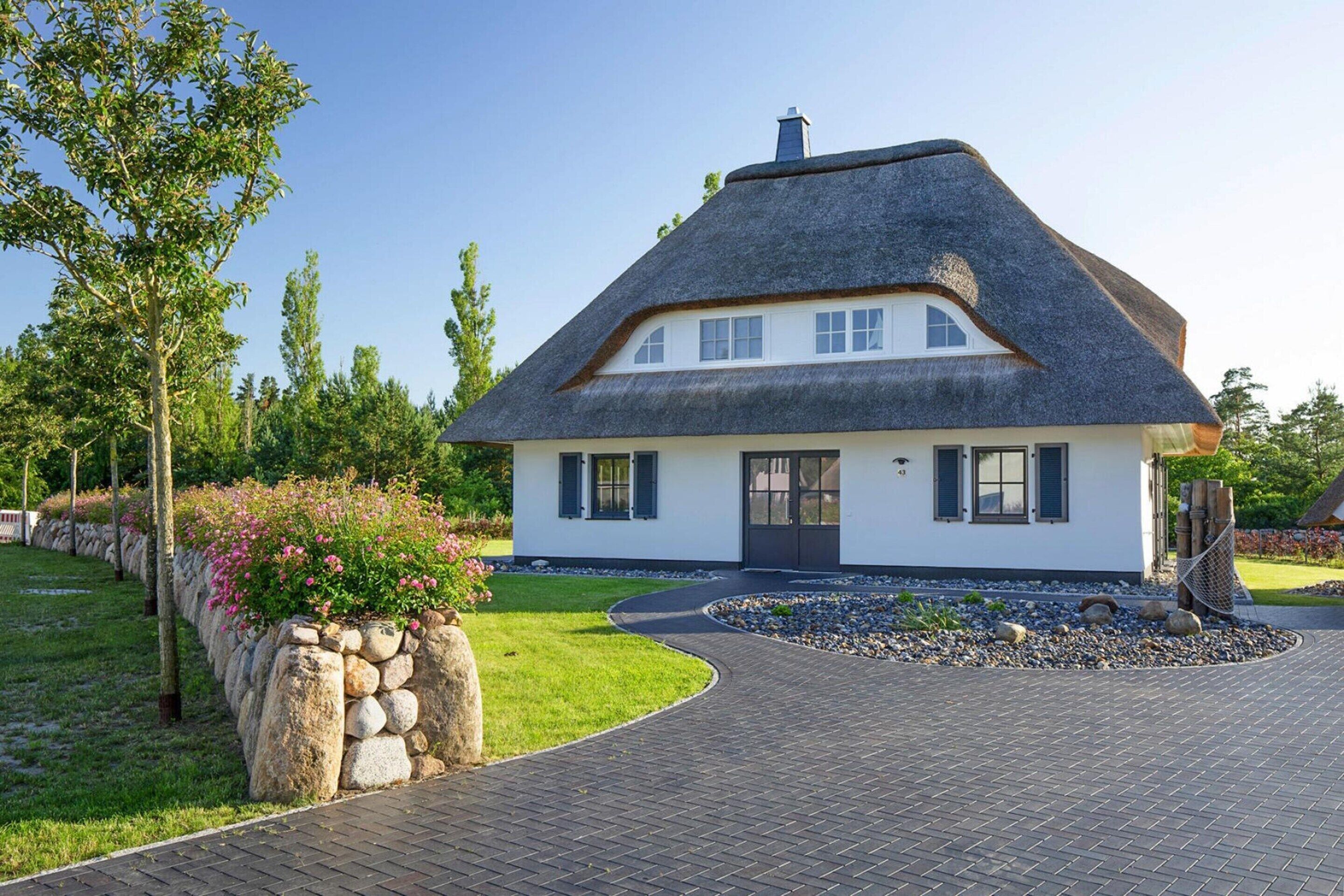 Une maison avec un toit de chaume, des murs extérieurs blancs et un mur de pierre orné de fleurs.