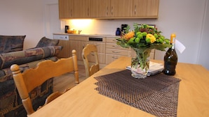En spiseplads med et træbord, stole, en vase med blomster og en flaske vin.