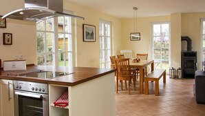 A kitchen with a central island, dining table, chairs, oven, and a built-in stove. - Ferienhaus in Wohlenberg Nahe der Ostsee (Klütz)