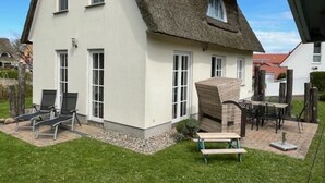 A house with a thatched roof, white exterior walls, and a small garden with outdoor furniture. - Ferienhaus in Wohlenberg Nahe der Ostsee (Klütz)