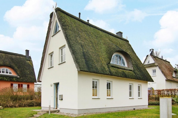 A white house with a steeply pitched roof, a small porch, and a window with a blue frame.