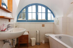 Um banheiro com pia branca, banheira, vaso sanitário e janela com detalhes azuis.