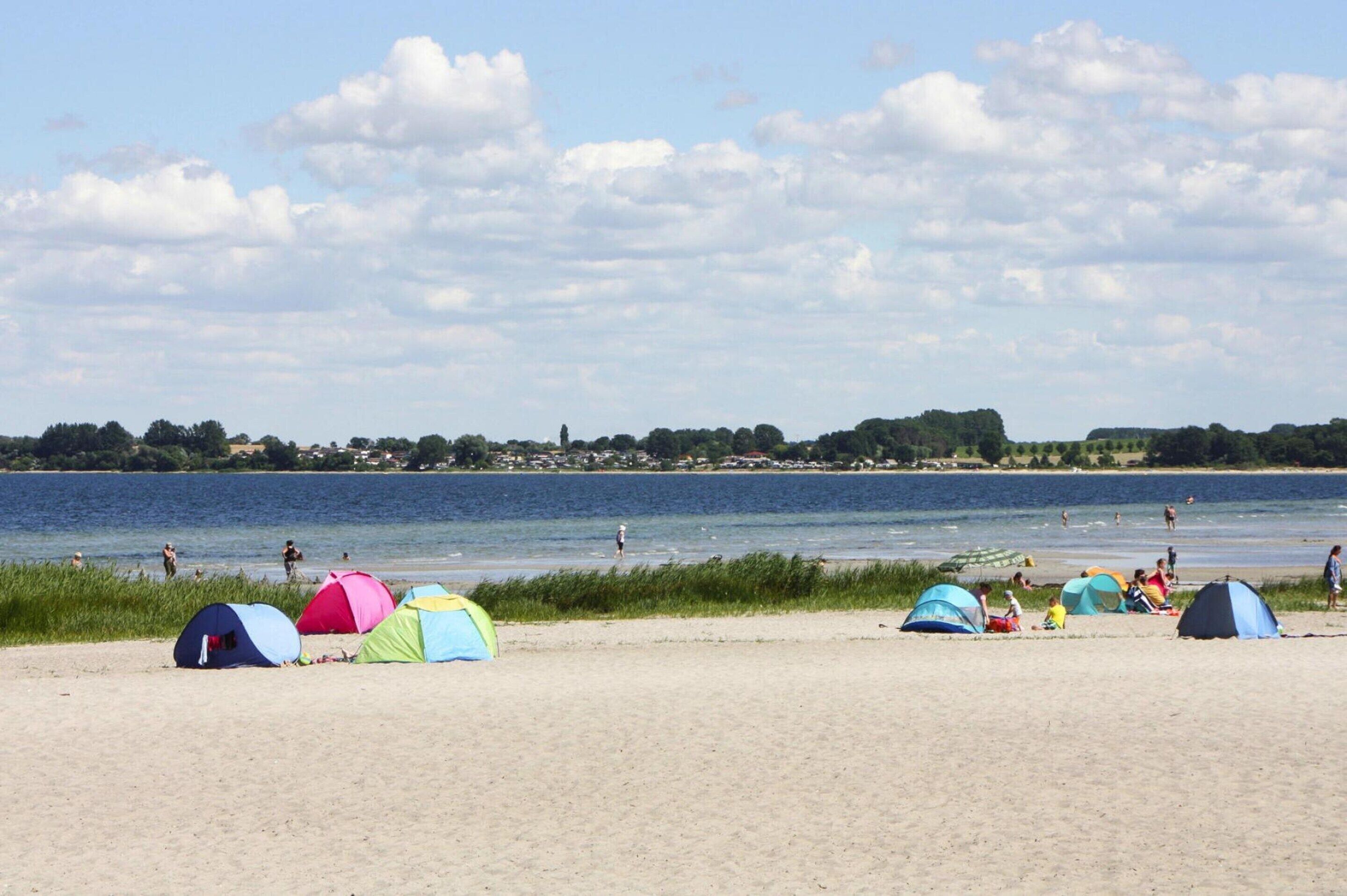 A beach with several colorful tents and a calm lake in the background.
