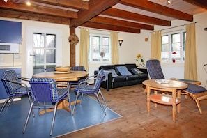 Ein gemütliches Wohnzimmer mit Holzboden, einem schwarzen Sofa, blauen Sesseln, einem Holztisch und einem Esstisch mit Stühlen.