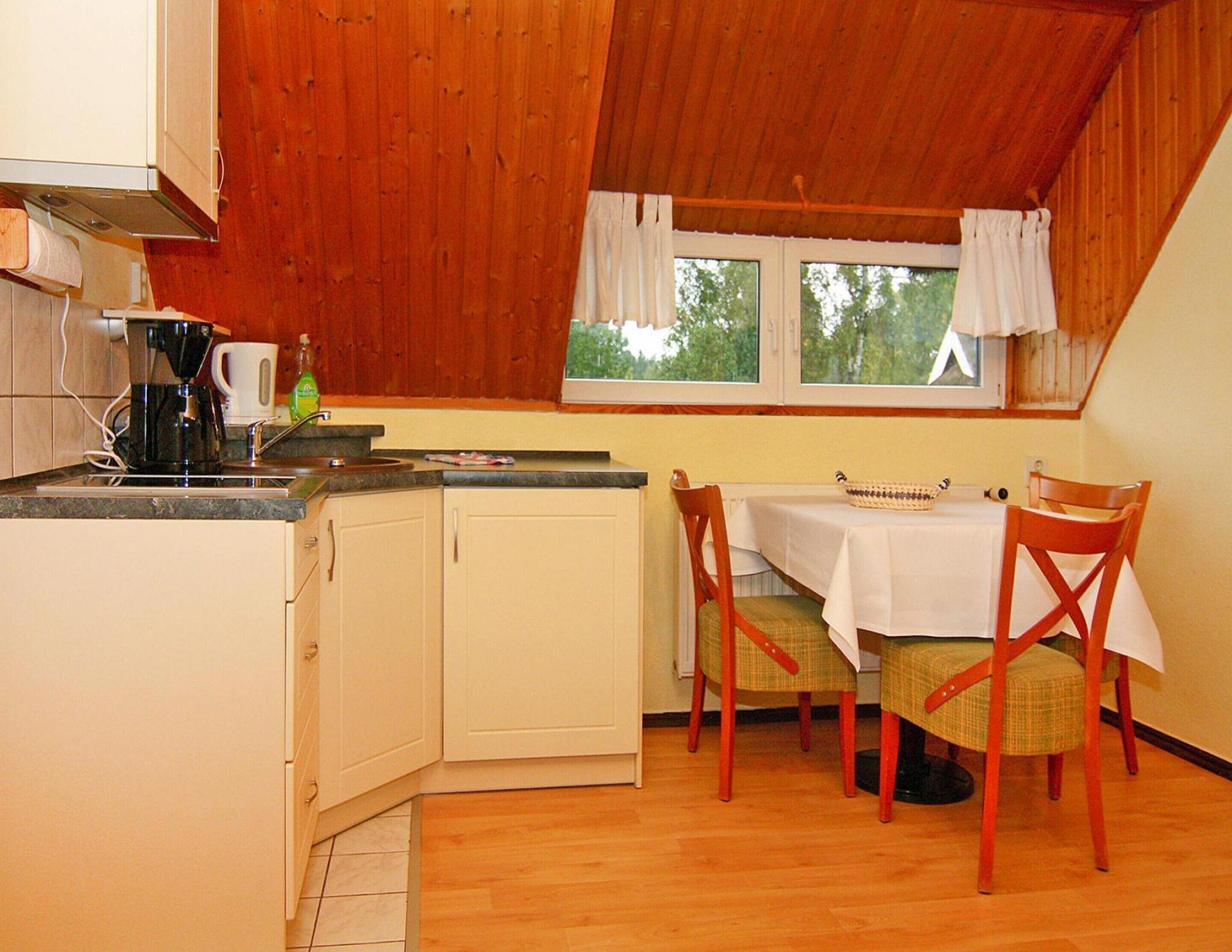 Una cocina con armarios de madera, una cafetera y una mesa de comedor con sillas.