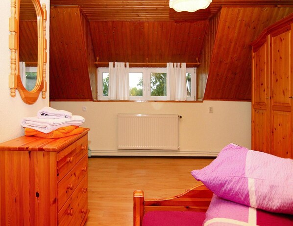 A wooden room with a bed, a dresser, a mirror, and a window with curtains. - Ferienwohnung mit Balkon am Bodstedter Bodden (Wieck auf dem Darss)