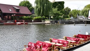 A rowboat with wooden chairs and tables, docked at a canal with a restaurant in the background. - Appartements mit Blick auf die Spree in Lubben (Lübben (Spreewald))