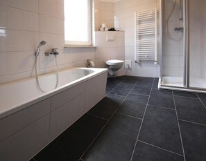 Une salle de bain moderne avec une baignoire sur pieds, des toilettes et une douche séparée par des parois en verre.
