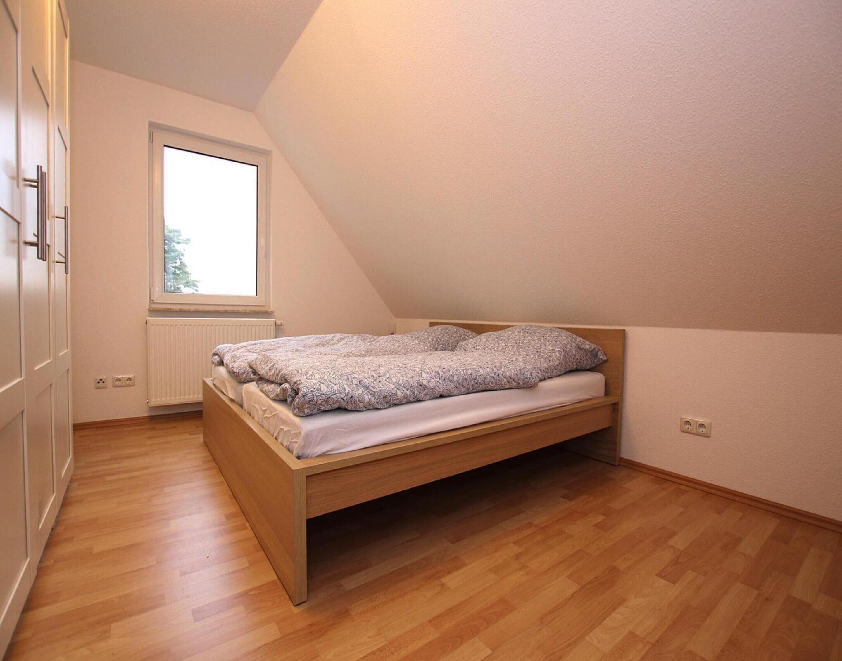 A single bed in a room with a sloped ceiling, a window, and a radiator.