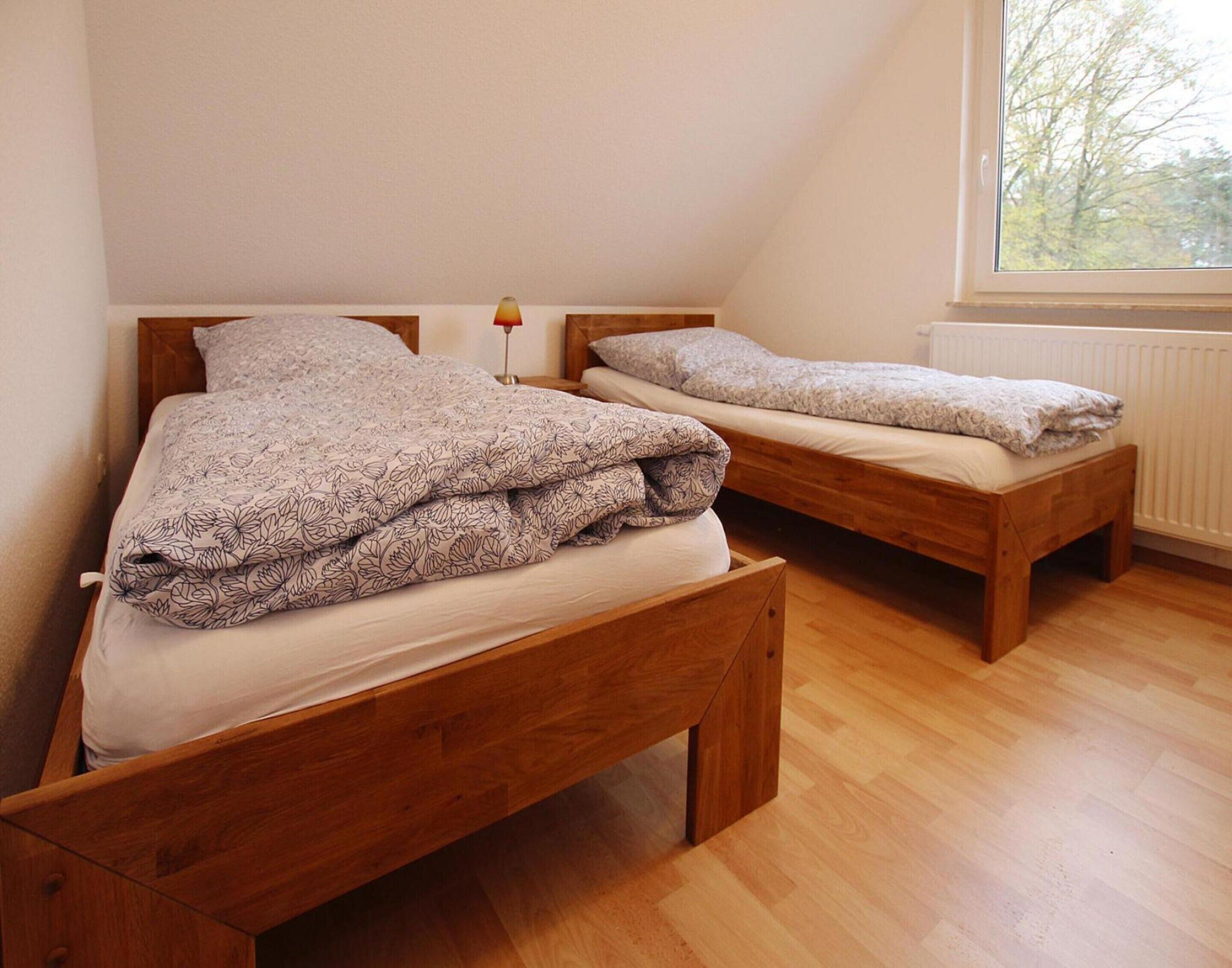 Deux lits en bois, recouverts de draps à motifs floraux, dans une pièce dotée d’une fenêtre et d’un radiateur.