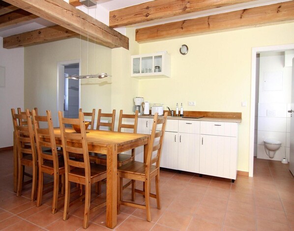 A dining area with a wooden table and chairs, a kitchen with white cabinets, and a tiled floor. - Ferienwohnung auf Usedom im Lepels Hof bis zu 8 P (Luetow)