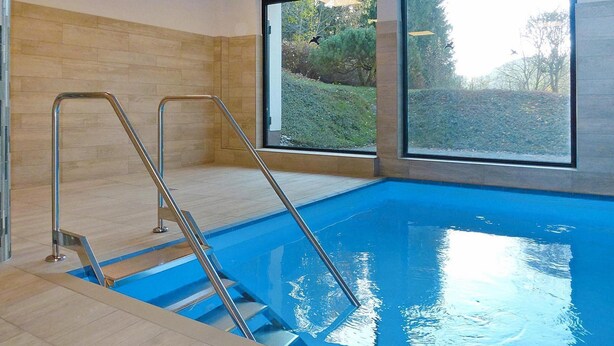 An indoor swimming pool with clear glass walls, metal ladders, and a view of greenery outside. - Studio in Winterberg Near Ski Slopes (Winterberg)