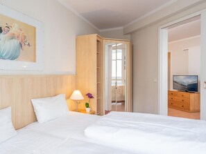 A hotel room with a bed, a nightstand with a lamp, a TV on a wooden cabinet, and a door leading to another room. - Komfortable Ferienwohnung im Seepark Sellin (Sellin)