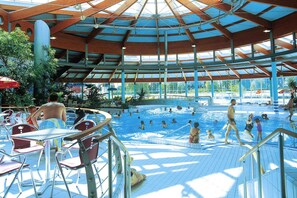 An indoor swimming pool with a covered roof, surrounded by red chairs and tables. - Komfortable Ferienwohnung im Seepark Sellin (Sellin)