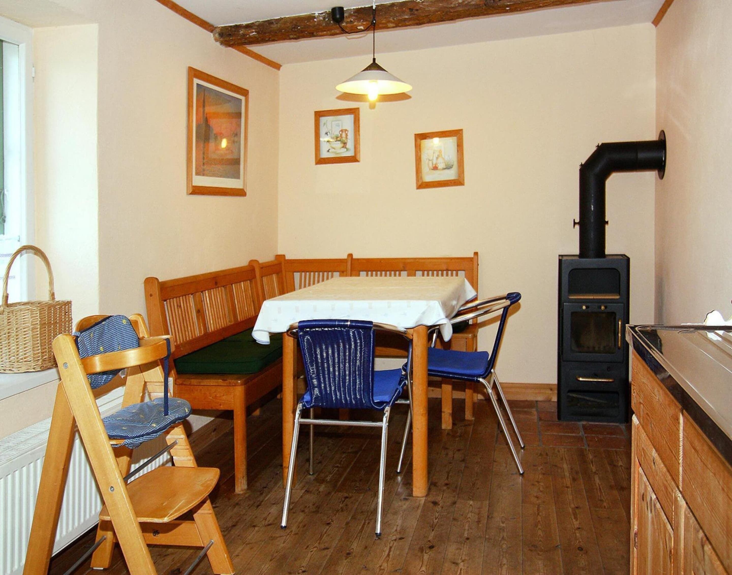 Una habitación acogedora con un banco de madera, una mesa con mantel blanco y un estufa de leña negra.