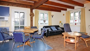 A cozy living room with a wooden floor, a black sofa, blue and white chairs, a wooden coffee table, and a dining table with chairs. - Reihenhaus Vieregge in Deutschland mit Terrasse (Neuenkirchen)