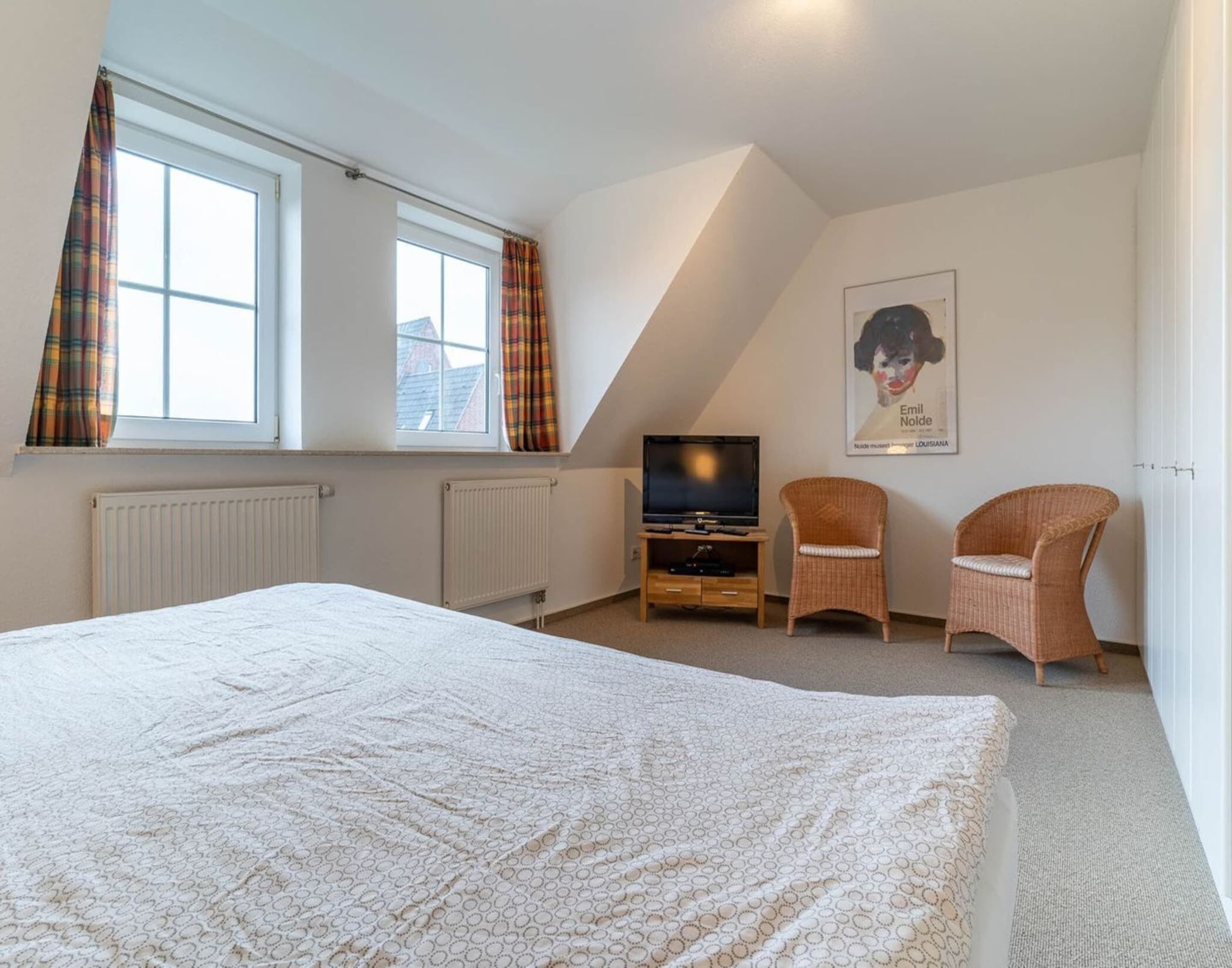Une chambre à coucher avec un grand lit, une télévision, deux fauteuils en osier et une affiche accrochée au mur.