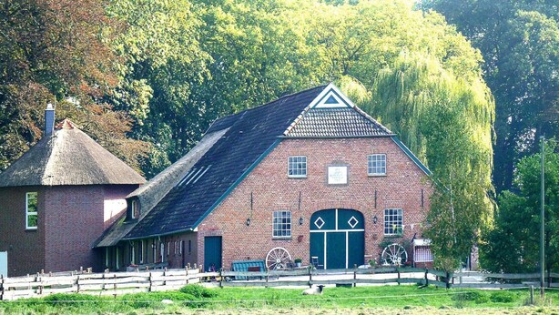 A traditional brick building with a thatched roof, a large wheel, and a green door. - Ferienhof Landhaus Markus, Suderschwei (Stadland)