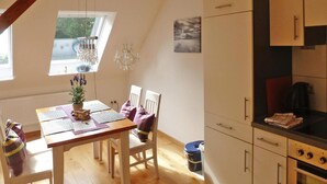A dining area with a wooden table, two chairs, a chandelier, and a view of the outdoors through a window. - Ferienhof Landhaus Markus, Suderschwei (Stadland)