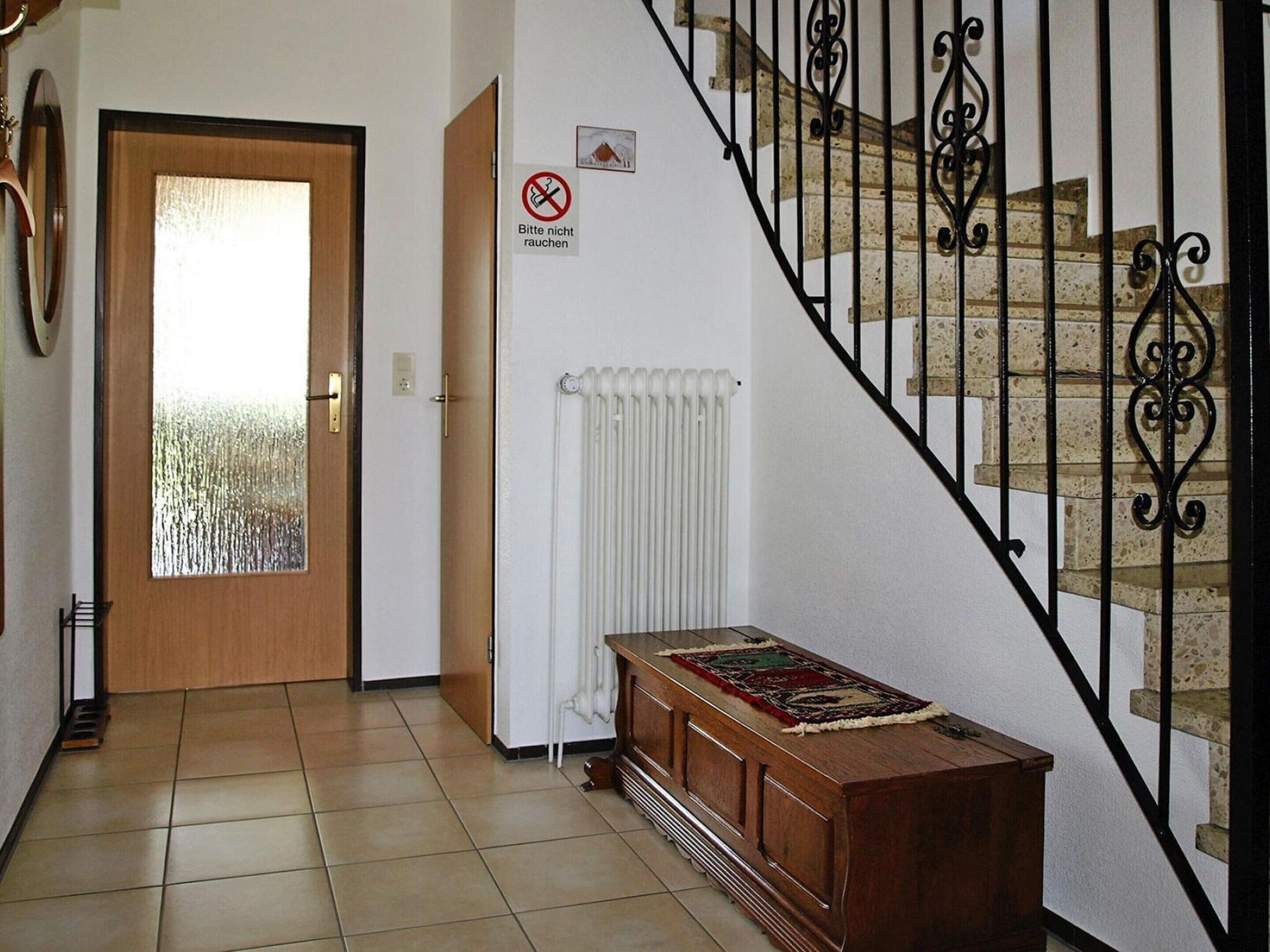 A hallway with a wooden door, a radiator, and a staircase with black railings.