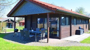 Un espace extérieur abrité, avec une table et des chaises, un barbecue et un bâtiment en bois doté d’un toit en pente.
