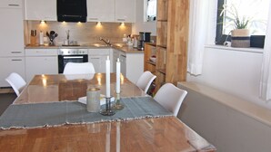 Une cuisine moderne avec des meubles blancs, une table à manger en bois décorée de bougies et une fenêtre agrémentée d’une plante.