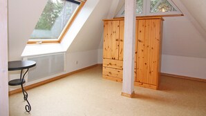 A room with a sloped ceiling, a window, a wooden cabinet, and a small table. - Doppelhaushalfte Ostseehaus II, Trassenheide (Trassenheide)