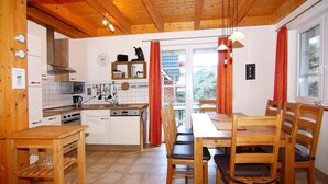 A kitchen with wooden cabinets, a stove, and a dining area with a table and chairs. - Doppelhaushalfte Ostseehaus II, Trassenheide (Trassenheide)