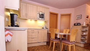 A compact kitchen with wooden cabinets, a microwave, a sink, and a dining area with two chairs.