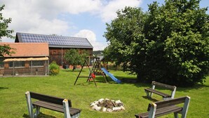 A grassy outdoor area with two wooden benches, a swing set, and a solar panel building in the background.