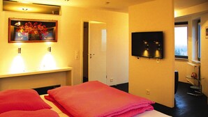 Et hotelværelse med en seng, et fjernsyn ophængt på væggen og et billede over sengen.