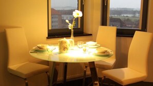 Et spiseområde med et rundt glasbord, hvide stole og en vase med blomster.