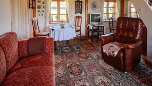 Ein gemütliches Wohnzimmer mit Holzboden, einem braunen Ledersessel, einem gemusterten Teppich und einem Fernseher auf einem Holzschrank.