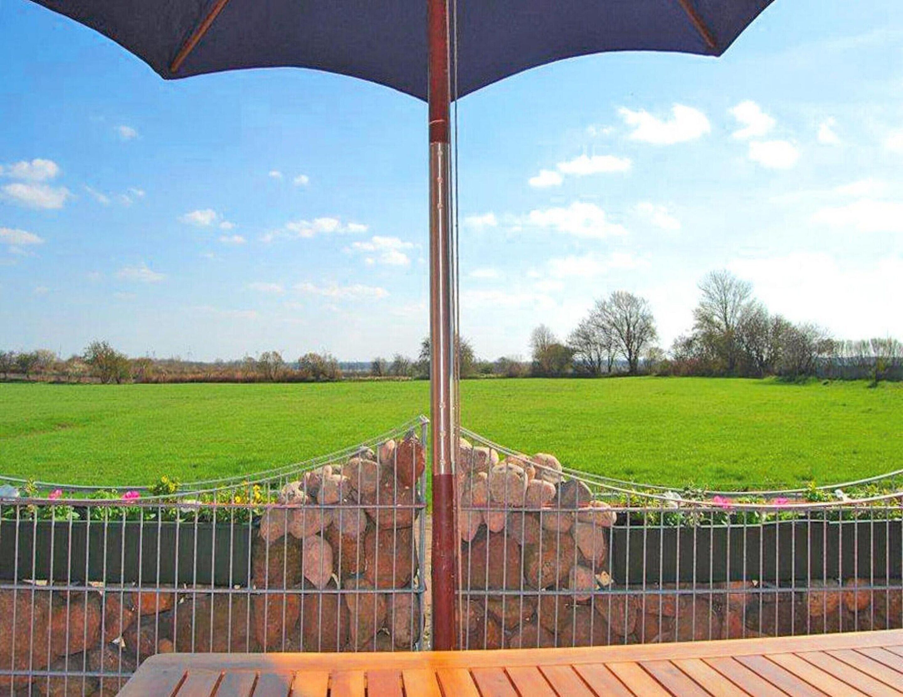 A patio with a metal railing, a stone wall, and a view of a green field under a clear sky.