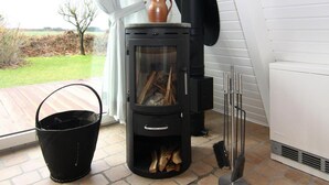 A wood-burning stove with a glass door, a black bucket, and a chimney. - Ferienhaus in Damp mit Terrasse (Damp)