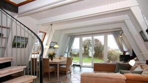 A spacious living area with a high ceiling, a dining table with chairs, a sofa, and a staircase with a railing. - Ferienhaus in Damp mit Terrasse (Damp)