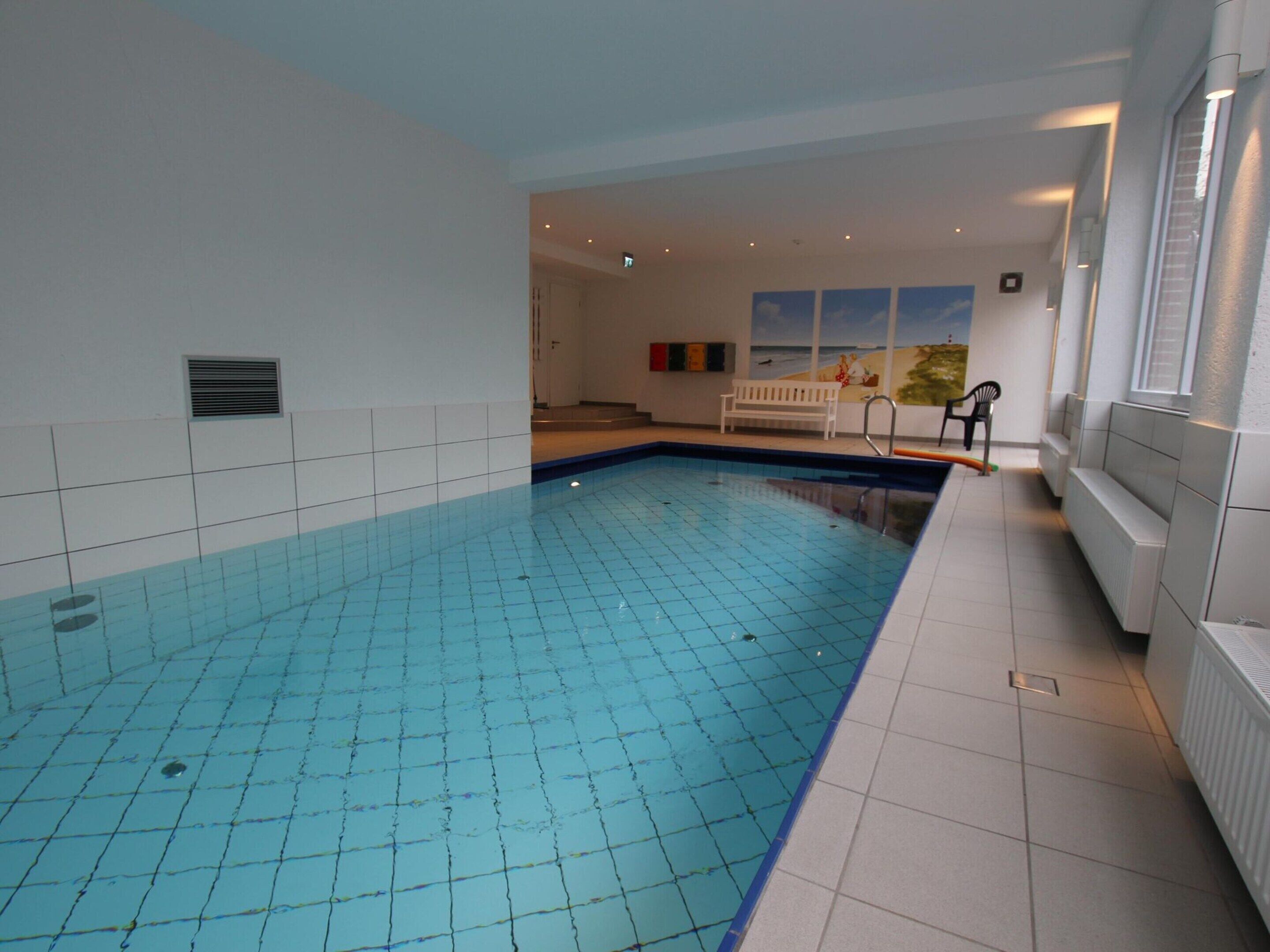 An indoor swimming pool with tiled walls and a bench in the background.